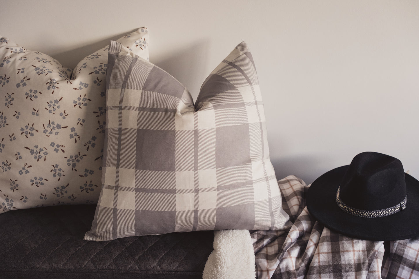 The Lil & Dot Wild Petal cushion and the Cozy Plaid cushion in Dusky Blue on a bench with a soft throw and a hat.