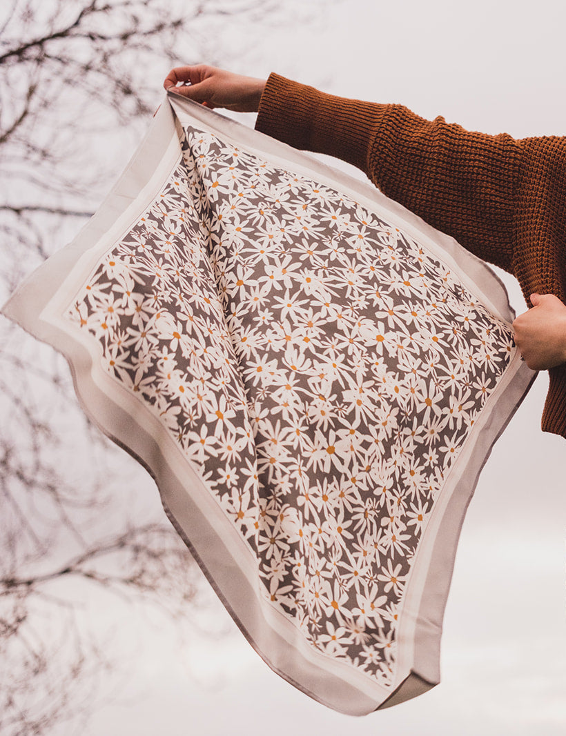 A woman holding the Lil & Dot hand painted Daisy Silk bandana in a cloudy english backdrop.