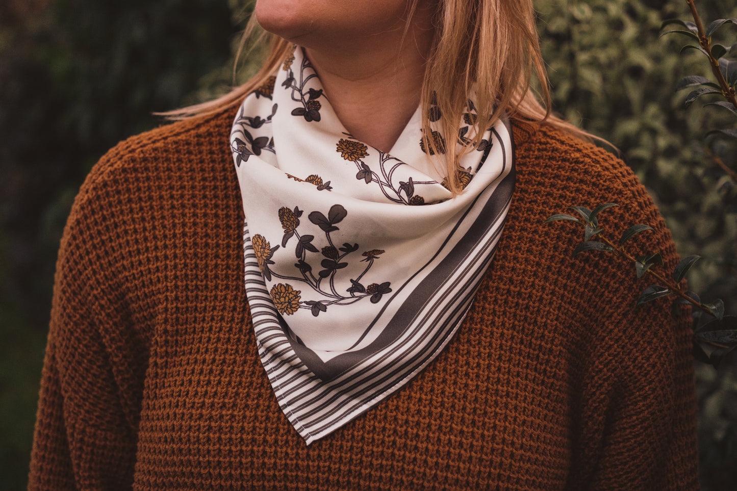 A woman in an ochre wolly jumper wearing the hand illustrated Clover Silk bandana.