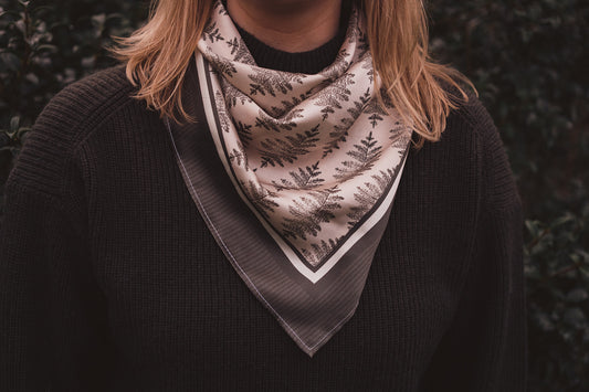 Image 2. A woman in a green knitted jumper wearing the hand illustrated Lil & Dot Fern Silk Bandana.