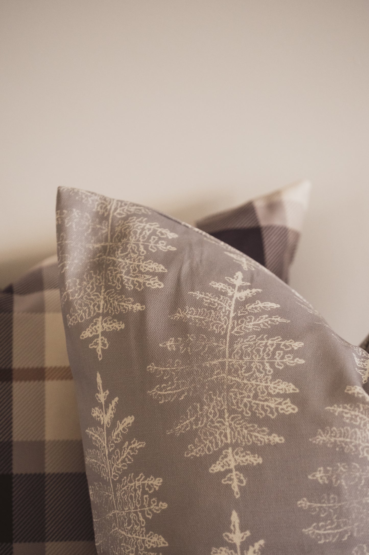 A close up of the Lil & Dot hand illustrated Fern Cushion in Dusky Blue and the Mocha Plaid Cushion.