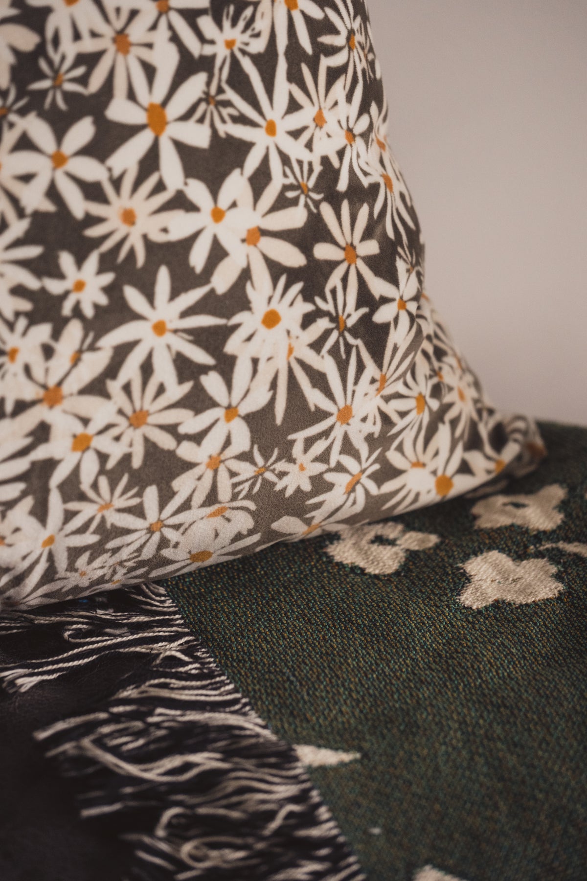 A close up of the Lil & Dot Daisy Cushion on a green botanical blanket.