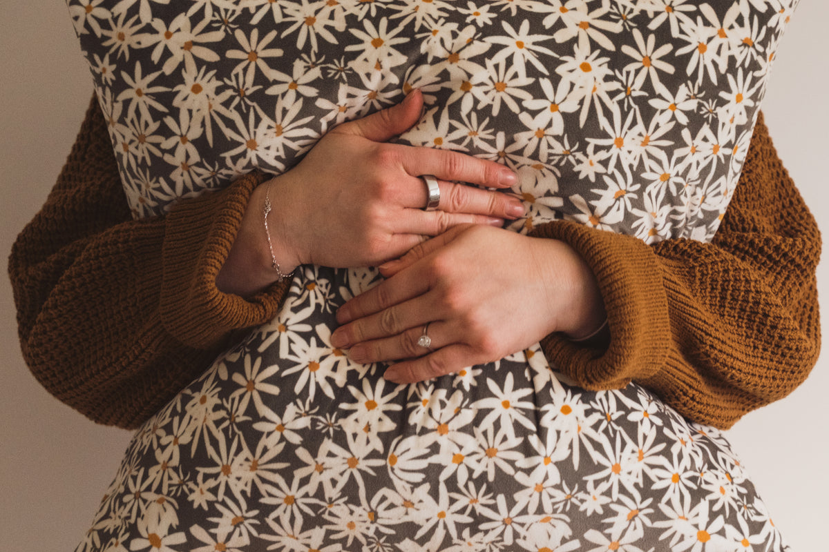 A woman wearing an ochre jumper with her hands wrapped around the Lil & Dot hand painted velvet Daisy Cuhsion.