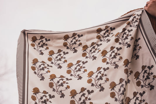 The hand illustrated Clover Bandana by Lil & Dot held up against the grey sky.