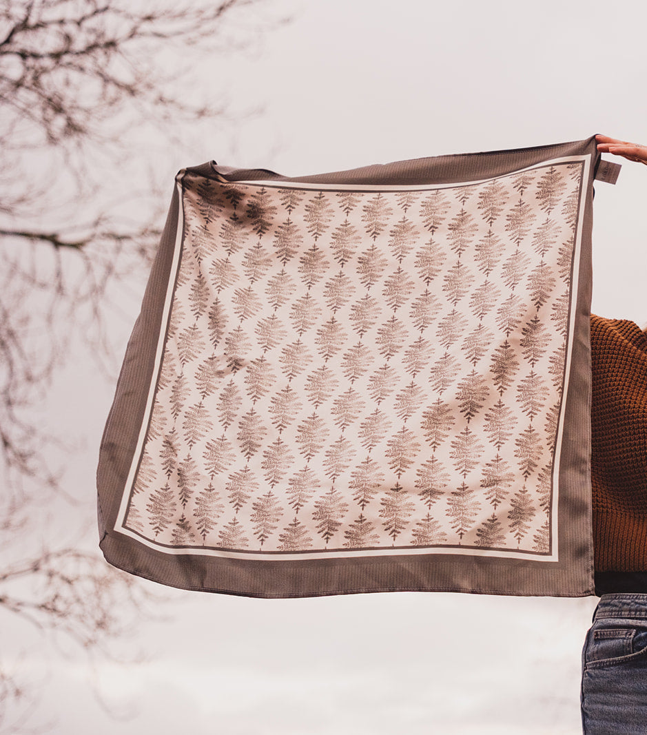 A woman holding the Lil & Dot hand illustrated Fern Silk Bandana in a cloudy english garden.